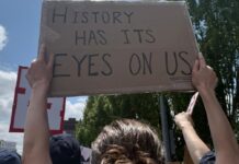 DHS busca aumentar castigos y arrestos contra manifestantes en propiedades federales Pancarta con la frase History Has Its Eyes On Us en la marcha No Kings Seattle