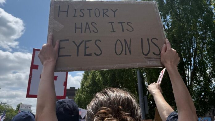 Pancarta con la frase History Has Its Eyes On Us en la marcha No Kings Seattle