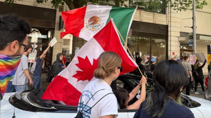 Personas manifestándose desde un vehículo ondean banderas de México y Canadá, en lo que para ellos es un símbolo de unidad internacional en defensa de los derechos civiles. Foto: para Latino Herald Maia Vázquez. Junio 14 del 2025. Participantes de la marcha No Kings Seattle ondean banderas de México y Canadá