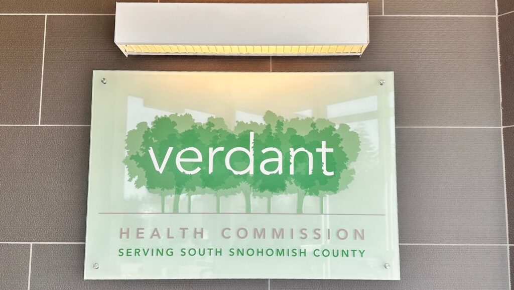 Letrero interior de Verdant Health Commission en Snohomish County, sobre fondo de árboles verdes.