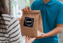 Uber Eats pagará casi $4.4 millones a más de 14,000 trabajadores en Seattle Trabajador de entrega entrega a una mujer una bolsa de comida con el logotipo de Uber.