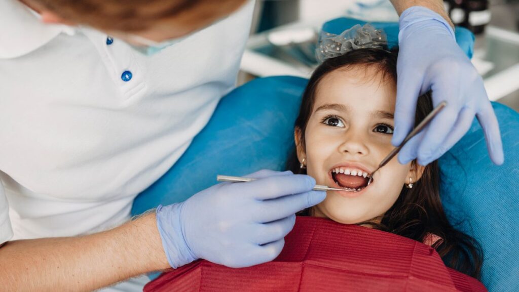 Un dentista revisa la boca de una niña pequeña en el sillón dental.