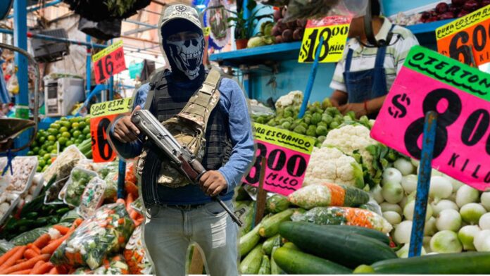 Sicario en el mercado Persona armada con rifle de asalto y rostro cubierto, en un mercado de frutas y verduras con carteles de precios visibles.