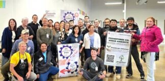 Programa Promotores del Medio Ambiente de WSU en el condado Snohomish Un grupo numeroso de personas sonríe y posa para una foto grupal en un evento de comunidad, sosteniendo letreros que promueven los programas "Promotores del Medio Ambiente" y "Latino Fix-It".