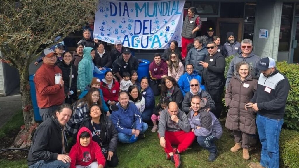 Varias personas posan para una foto grupal al aire libre. Detrás de ellos cuelga un banner que dice "Día Mundial del Agua" con huellas de manos azules.
