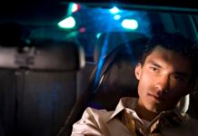 Seattle refuerza controles de DUI con patrullajes especiales durante diciembre Hombre hispano en el asiento de un vehículo con luces rojas y azules de un vehículo policial detrás de él.