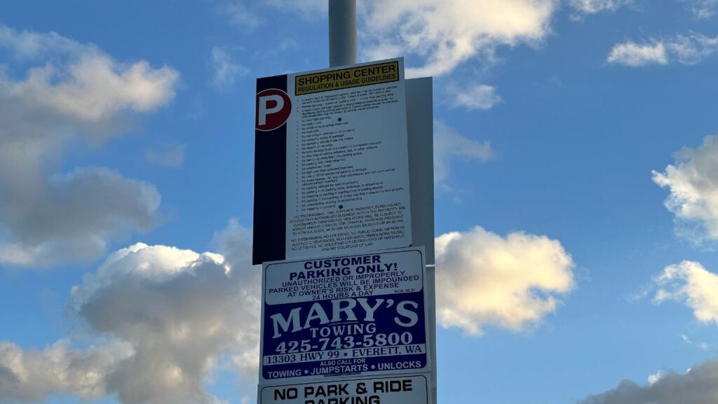 Señal de Mary’s Towing en lote privado cerca de la estación de tren ligero Lynnwood, con el tren de Sound Transit al fondo © Latino Herald.