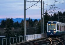 Extensión del tren ligero facilitará acceso al campus de Highline College y al aeropuerto SeaTac Tren ligero de Sound Transit rumbo a Federal Way sobre una vía elevada, con montañas al fondo al atardecer