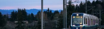Tren ligero de Sound Transit rumbo a Federal Way sobre una vía elevada, con montañas al fondo al atardecer