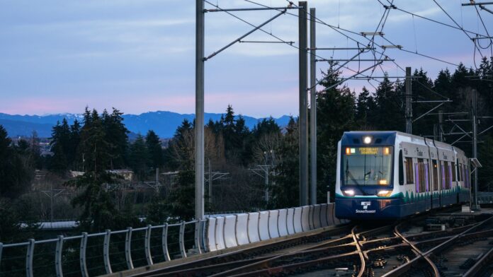 Tren ligero de Sound Transit rumbo a Federal Way sobre una vía elevada, con montañas al fondo al atardecer