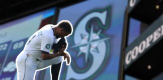 Octubre es proclamado como el Mes de los Mariners en Seattle Jugador de los Seattle Mariners arrodillado en el campo con la gorra en el rostro, frente a una gran pantalla que muestra el logotipo del equipo.