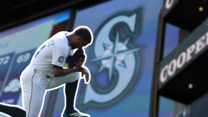 22-general-.jpg Jugador de los Seattle Mariners arrodillado en el campo con la gorra en el rostro, frente a una gran pantalla que muestra el logotipo del equipo.