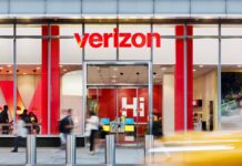 Verizon anuncia el mayor recorte de empleos en su historia Tienda de Verizon vista desde el exterior, con el logotipo rojo visible y clientes entrando y saliendo del establecimiento.