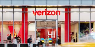 Verizon anuncia el mayor recorte de empleos en su historia Tienda de Verizon vista desde el exterior, con el logotipo rojo visible y clientes entrando y saliendo del establecimiento.