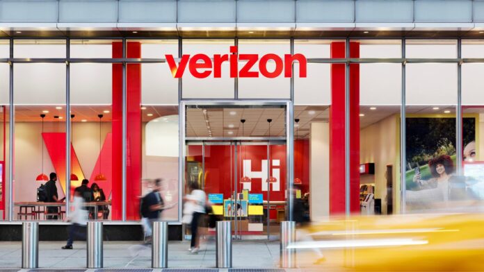 Tienda de Verizon vista desde el exterior, con el logotipo rojo visible y clientes entrando y saliendo del establecimiento.