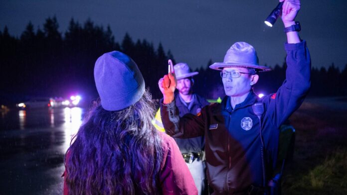 Una mujer realiza una prueba ocular de sobriedad mientras un oficial sostiene una linterna en un control policial nocturno.