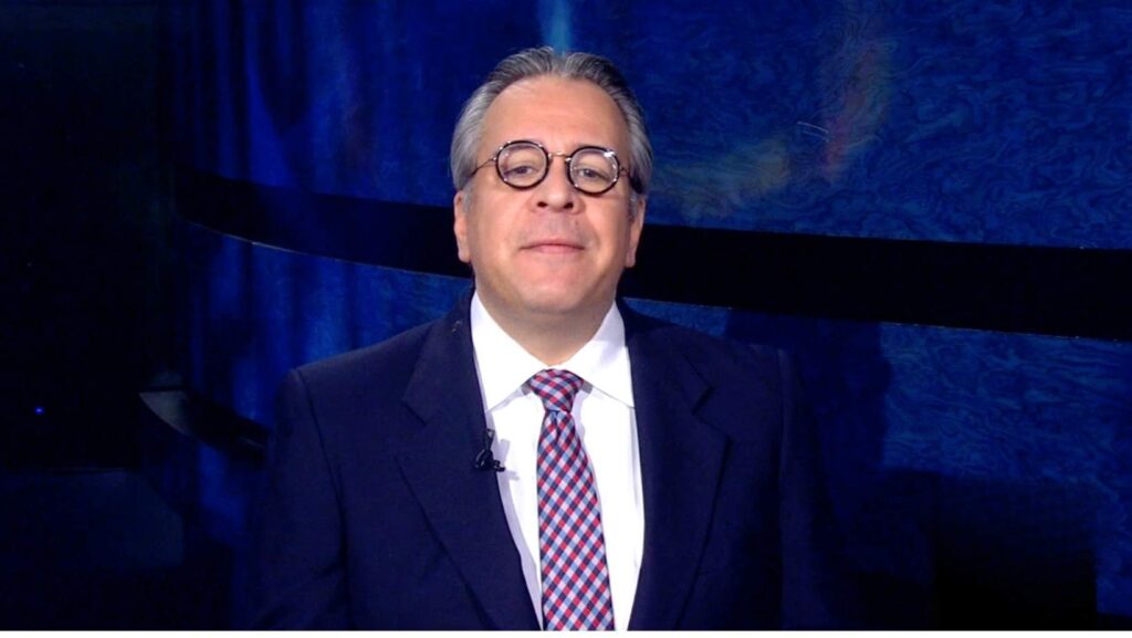 José Luis González, periodista y productor de noticias aparece en un set de noticias usando traje y corbata.