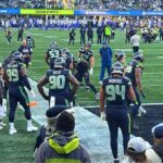 Seahawks derrotan a los Rams y avanzan al Super Bowl LX Seattle Seahawks realizando ejercicios de calentamiento en la línea lateral del campo en el estadio Lumen Field antes del partido contra Los Angeles Rams, rodeados de aficionados y personal del equipo.