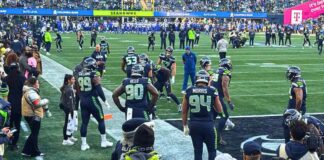 Seahawks derrotan a los Rams y avanzan al Super Bowl LX Seattle Seahawks realizando ejercicios de calentamiento en la línea lateral del campo en el estadio Lumen Field antes del partido contra Los Angeles Rams, rodeados de aficionados y personal del equipo.