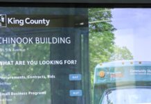 El condado King comenzará a aplicar el mandato de regreso a la oficina Pantalla informativa en el lobby del edificio Chinook de King County que muestra servicios y ubicación de oficinas.