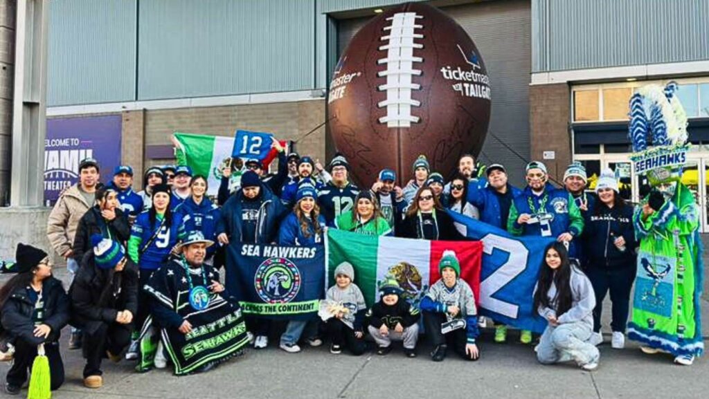 Grupo de aficionados del Sea Hawkers Latin America Club posando frente a una escultura gigante de un balón de fútbol americano en la entrada del estadio Lumen Field antes del juego entre los Seattle Seahawks y Los Angeles Rams, el 25 de enero.