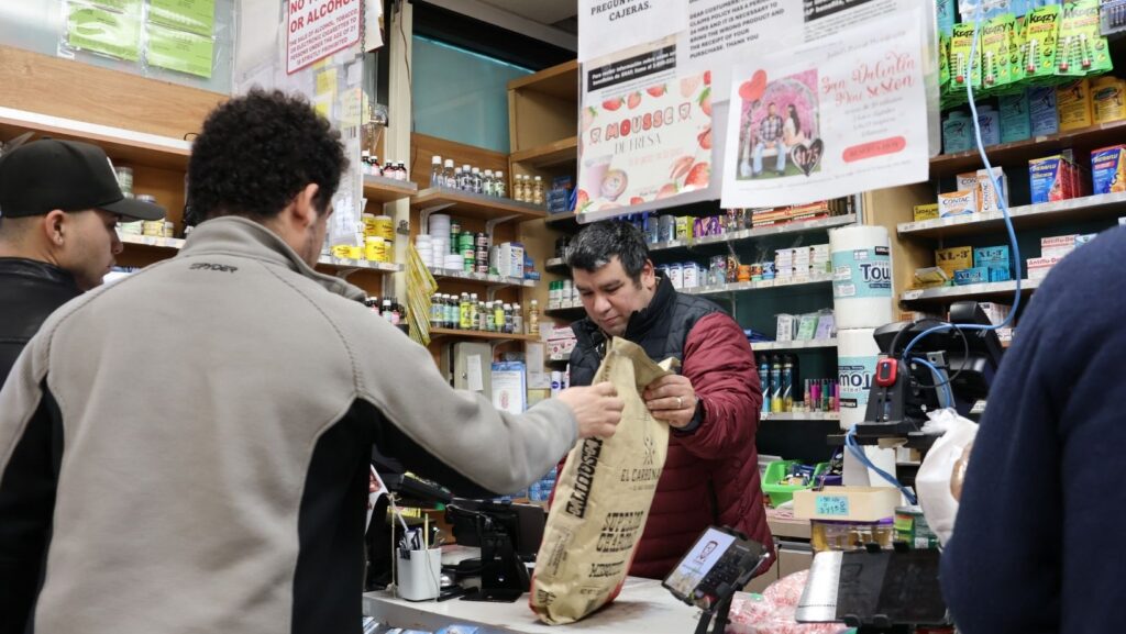 Tony Hernández, con chamarra roja y negra, atiende a un cliente en la caja del supermercado Los Gavilanes en Everett.