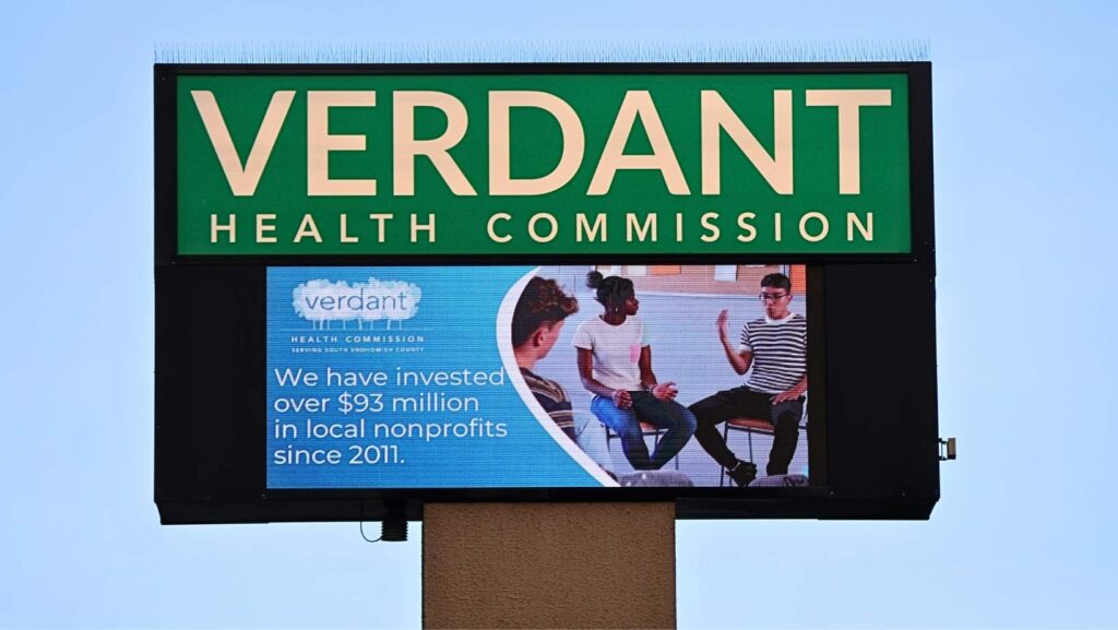 Pantalla digital de la Verdant Health Commission mostrando mensaje sobre inversión de más de 93 millones de dólares en organizaciones locales desde 2011