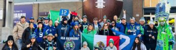 Miembros del club Sea Hawkers Latin America posan frente al estadio de los Seattle Seahawks con banderas de México y el banner oficial del club