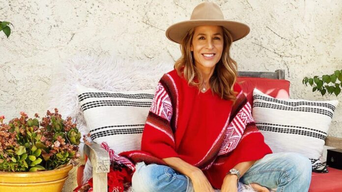 Sylvia Villagrán sentada al aire libre con sombrero y poncho rojo, sonriendo en un entorno relajado.