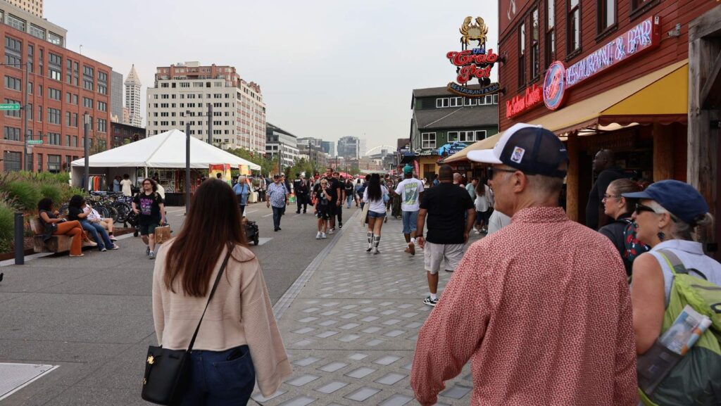 Personas caminando por el paseo renovado de Waterfront Park con restaurantes y puestos temporales durante el evento inaugural.