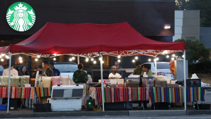 Puesto de comida en Lynnwood Puesto de comida instalado en una acera frente a Highway 99 en Lynnwood, Washington, con vendedores y clientes bajo una carpa roja durante la noche.