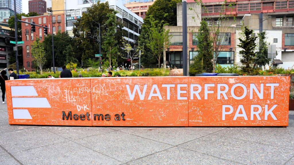 Letrero naranja de “Waterfront Park – Meet Me at” cubierto con firmas y mensajes durante la inauguración en Seattle.