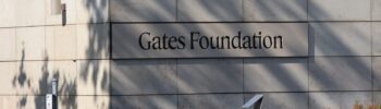 Fachada del edificio de la Fundación Gates con el letrero visible en la pared exterior y el número 500 en la esquina, rodeado de vegetación en Seattle.