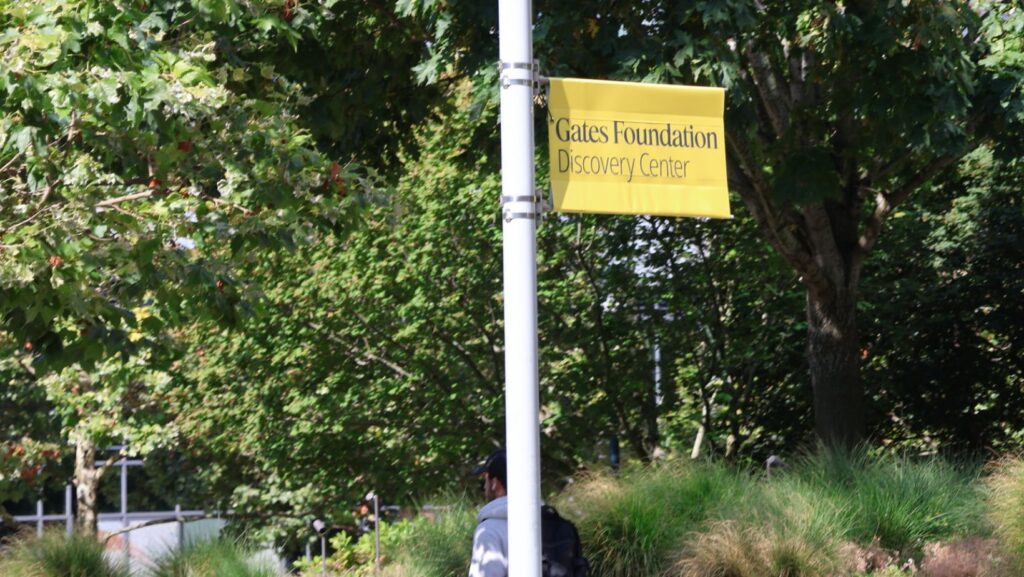 Bandera amarilla con el texto “Gates Foundation Discovery Center” colocada en un poste, rodeada de árboles y vegetación en Seattle.