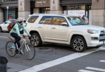 Seattle: Nuevo carril para bicicletas busca facilitar la llegada al malecón Un ciclista espera la luz verde junto a una camioneta en Yesler Way y 1st Ave S, donde el SDOT está instalando un nuevo carril bidireccional protegido – Foto cortesía del SDOT