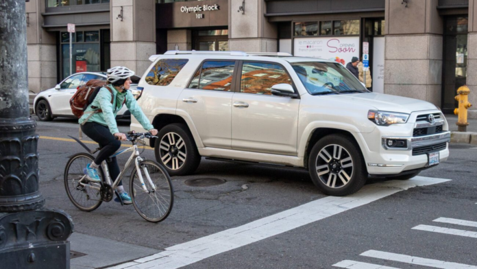Un ciclista espera la luz verde junto a una camioneta en Yesler Way y 1st Ave S, donde el SDOT está instalando un nuevo carril bidireccional protegido – Foto cortesía del SDOT