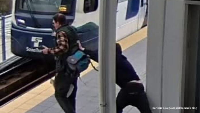 Captura de cámara de seguridad en la estación Northgate de Seattle que muestra a un hombre detrás de otro pasajero junto a las vías mientras llega un tren de Sound Transit.
