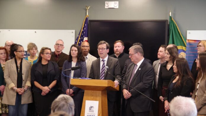 El gobernador Bob Ferguson habla en un podio acompañado por la alcaldesa de Everett, Cassie Franklin, y otros líderes locales y estatales durante un evento sobre vivienda en HopeWorks Station, en Everett, Washington, el 27 de marzo de 2026.