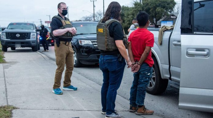 Arrestos de ICE rompen record: 50,000 en julio, la cifra más alta durante el mandato de Trump Agentes de HSI detienen a un hombre esposado junto a una camioneta blanca durante un operativo en la calle.