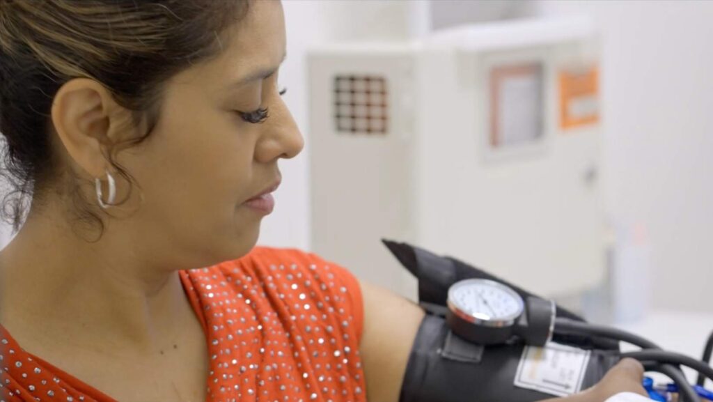 Mujer hispana mientras le toman la presión arterial en una consulta médica.