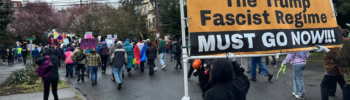 Manifestantes marchan por una calle de Seattle durante la Marcha de Mujeres del 8 de marzo mientras una persona sostiene un gran cartel de protesta contra Donald Trump entre la multitud.