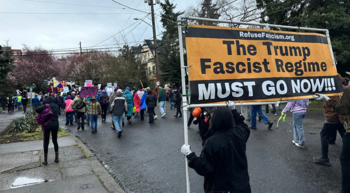 Marcha en apoyo a los derechos de las mujeres reúne a cientos en Seattle Manifestantes marchan por una calle de Seattle durante la Marcha de Mujeres del 8 de marzo mientras una persona sostiene un gran cartel de protesta contra Donald Trump entre la multitud.