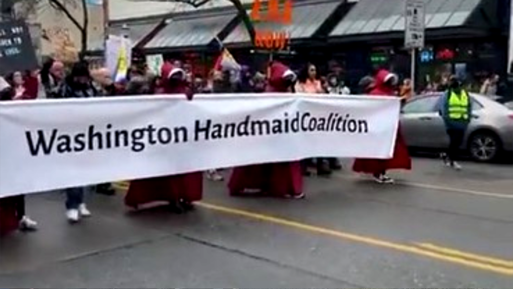 Personas vestidas con túnicas rojas inspiradas en The Handmaid’s Tale sostienen una pancarta que dice “Washington Handmaid Coalition” mientras participan en la Marcha de Mujeres del 8 de marzo en Seattle.