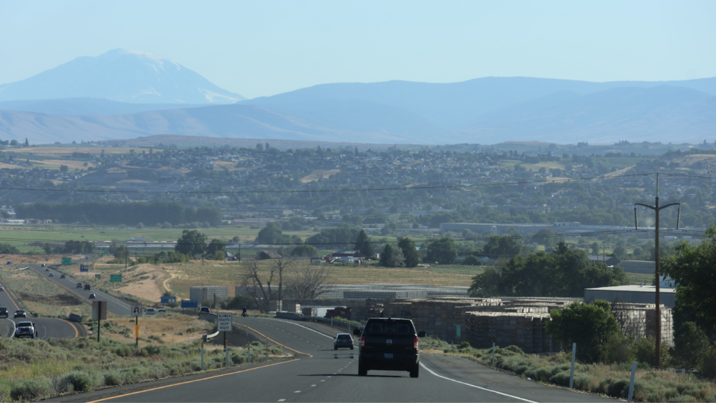 Carretera atravesando el valle de Yakima, con vista a zonas agrícolas y montañas al fondo, en un día despejado.