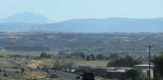 Demandan a empresa agrícola de Yakima por visas de trabajadores temporales Carretera atravesando el valle de Yakima, con vista a zonas agrícolas y montañas al fondo, en un día despejado.