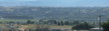 Carretera atravesando el valle de Yakima, con vista a zonas agrícolas y montañas al fondo, en un día despejado.