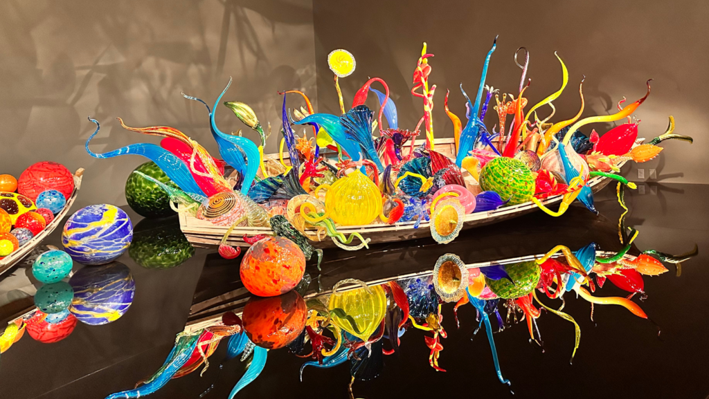 Vibrante instalación de vidrio de Dale Chihuly exhibida en Chihuly Garden and Glass, donde formas dinámicas y colores intensos crean un efecto visual reflejado sobre una superficie negra pulida.