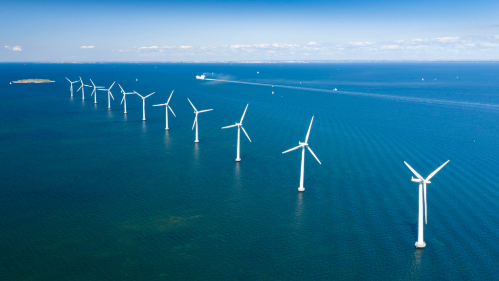 Turbinas eólicas marinas alineadas en el océano generan energía renovable bajo un cielo despejado.