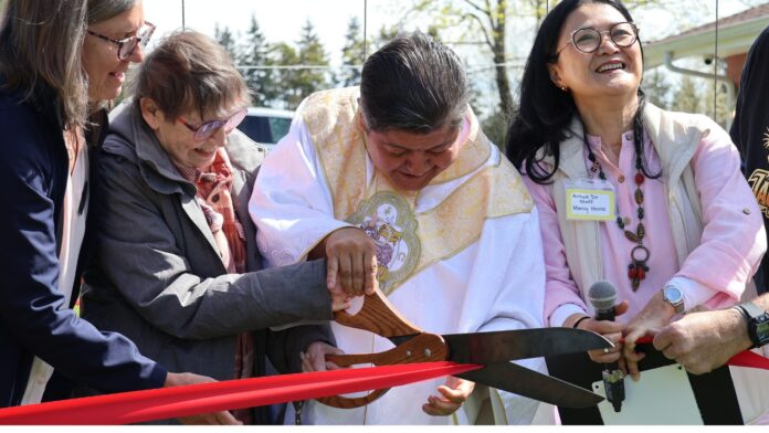 Corte de listón en la inauguración del jardín comunitario de Mercy House en Mountlake Terrace con sacerdote y organizadores.