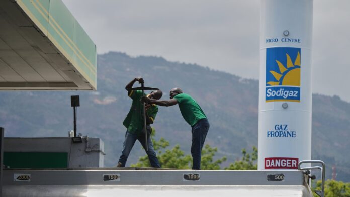 Precios del Petróleo afectan a Haití Trabajadores manipulan equipo en una estación de combustible con un tanque de gas propano al fondo, en medio de un entorno montañoso en Haití.